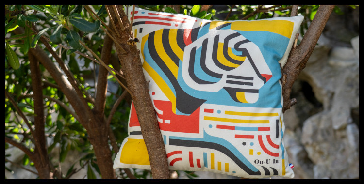 Coussin "Un Tigre à La Plage" de la marque marseillaise On-U-In, fabriqué en France, 100% coton. Le thème Un Tigre à La Plage représente un félin stylisé . La photo est prise dans un jardin près de la plage du prophète, derrière le bord de mer de la corniche, à Marseille.